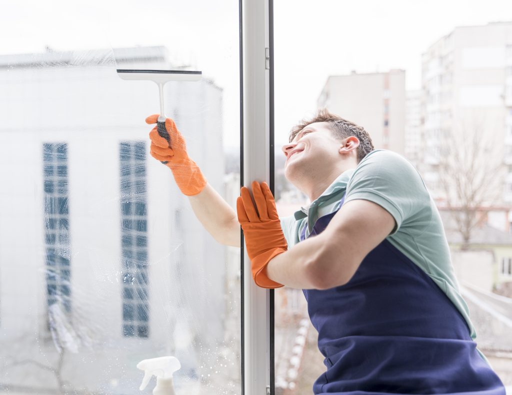 Fensterreiniger säubert Glas mit Handschuhen und Reinigungsmittel.